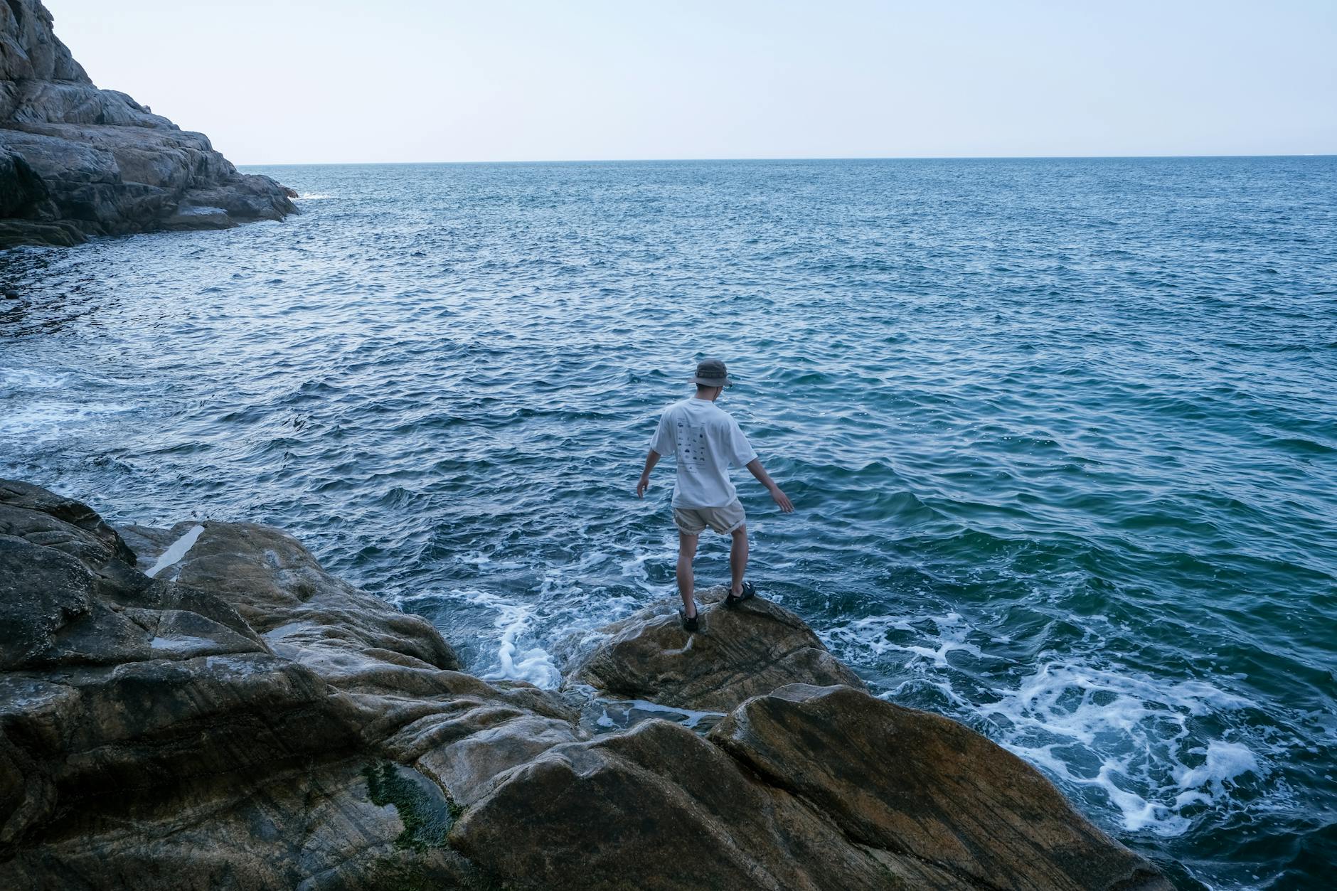 Person explores the rocky seashore while enjoying the serene ocean view.