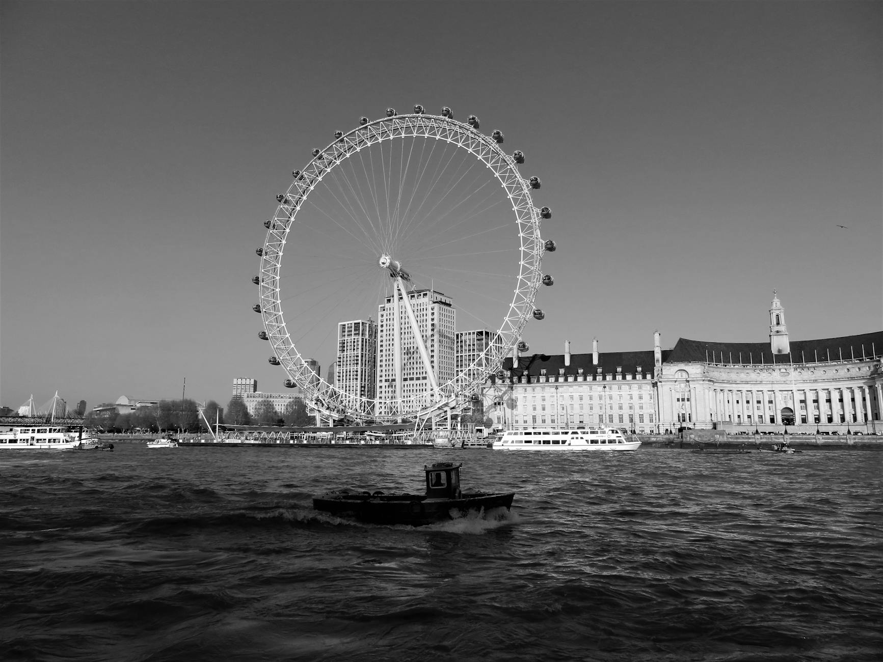 Monochrome view of the London Eye and riverside with a boat on the River Thames.
