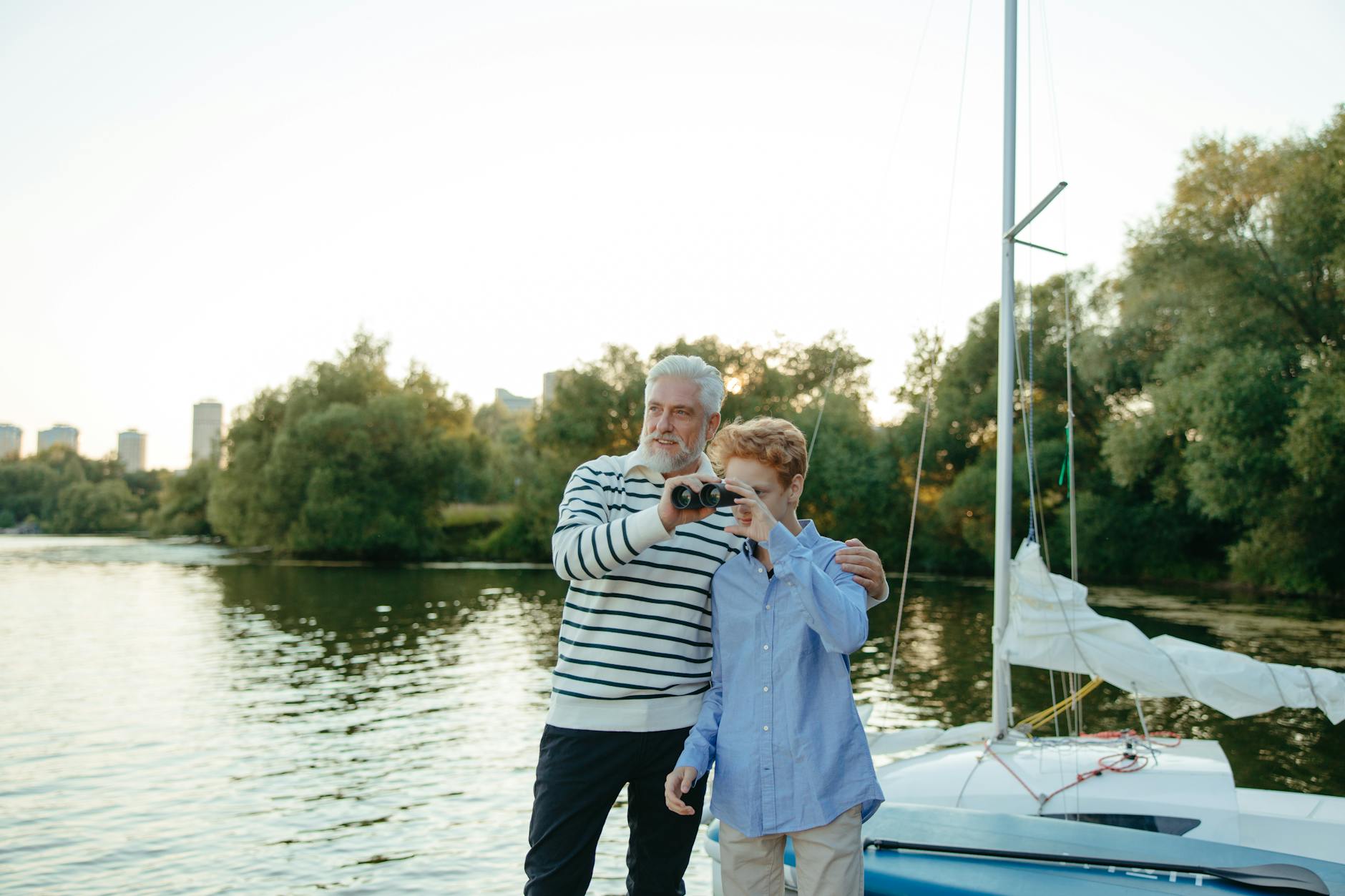 Elderly man and young boy bonding on a sailboat while exploring with binoculars.