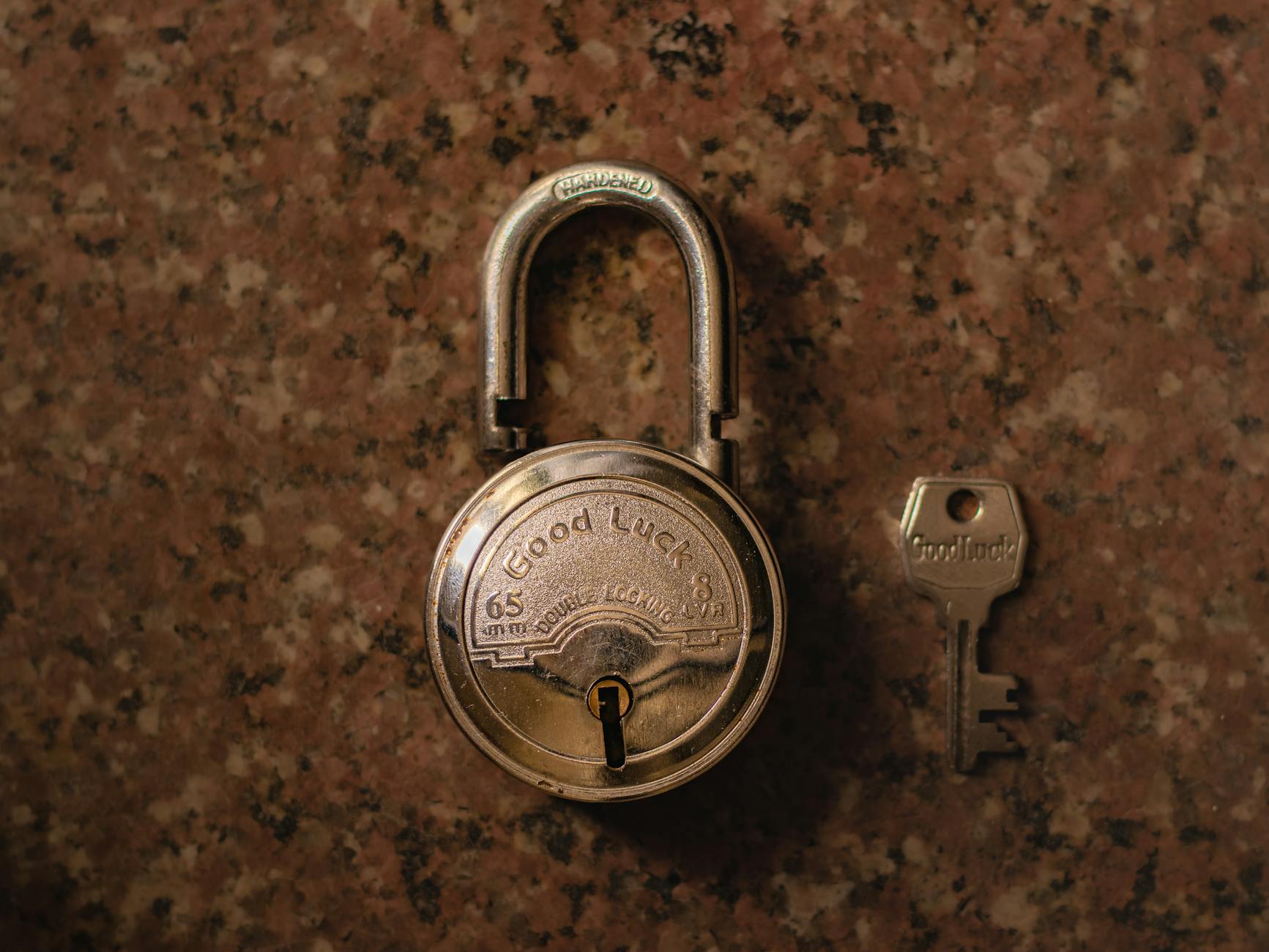 A close-up view of a vintage padlock with its key on a stone surface.